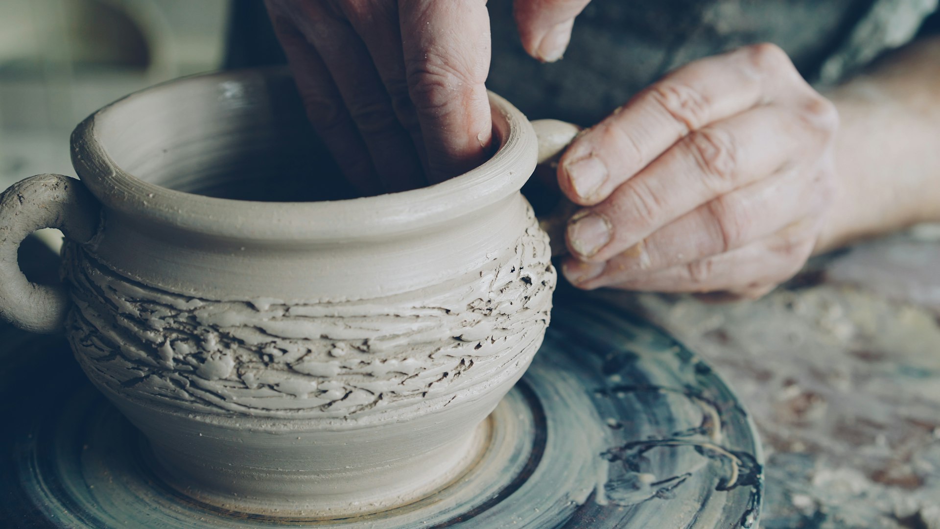 Hands sculpt a clay pot on the potter's wheel.